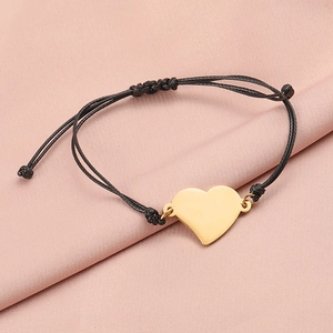 Macro detail of gold heart pendant on black braided rope bracelet with silk texture