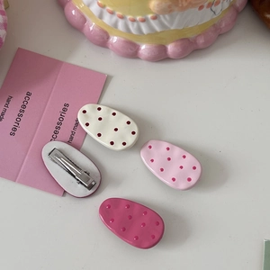 Detailed view of hair clips in white and pink polka dot patterns on a white background