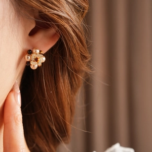 Close-up of floral stud earring with white pearls and tiger eye stone on model
