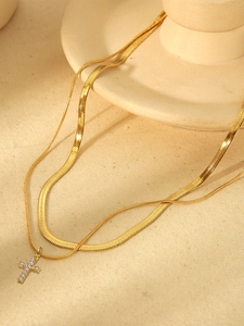 Detail of a layered gold necklace featuring a flat snake chain and gemstone cross pendant