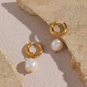 Détail d'une boucle d'oreille créole en or 18 carats avec perle baroque sur pierres