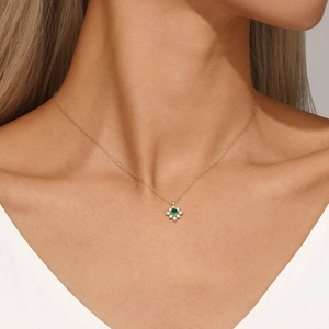 Detail of a floral gold necklace with a green gemstone worn on a model's neck