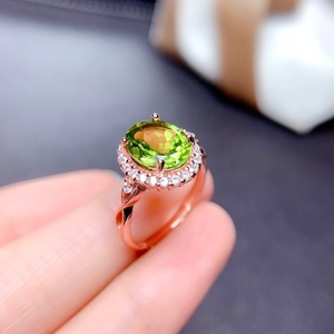 Oval green peridot ring in rose gold with halo diamond accents on a finger
