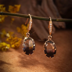 Macro shot of gold dangle earrings featuring oval purple gemstones and zircon accents