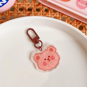 Pink acrylic bear keychain with brown metal clasp on a decorative white ceramic plate