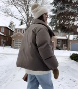 Detail of oversized brown winter puffer jacket in a snowy outdoor street setting