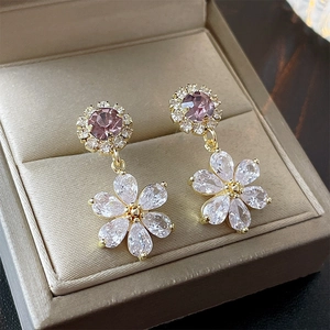Detailed macro of gold flower earrings with purple and clear zircon stones in a jewelry box