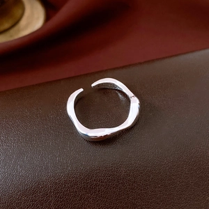 Detail view of irregular wavy silver ring on brown leather base with minimalist design