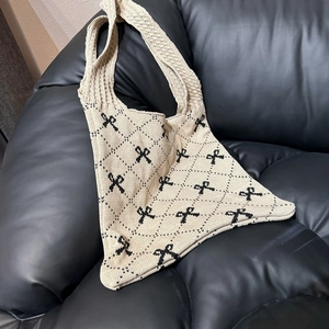 Detail der beige gestrickten Tragetasche mit schwarzem Karomuster und Schleifenmotiv