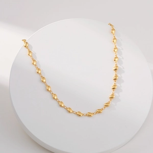 Polished gold bean link necklace with oval beads on white display stand, minimalist jewelry