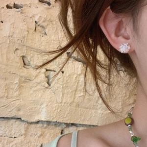 Close-up of crystal flower stud earring worn by model against a vintage beige wall