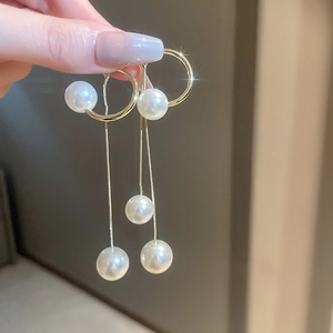 Close-up of golden geometric earrings with long pearl tassels and elegant metallic details