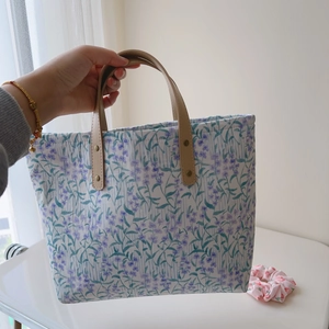 Détail d'un sac cabas en coton à fleurs avec anses en cuir et rivets dorés brillants
