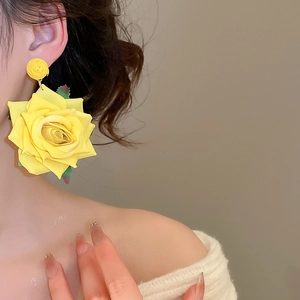 Detailed view of yellow fabric rose earrings with silk texture on model