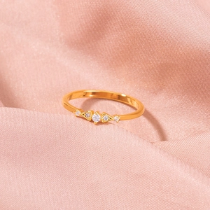 Detail of gold ring featuring five cubic zirconia stones on pink satin fabric