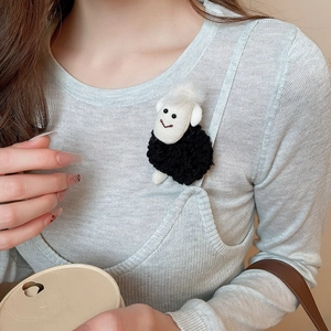 Close-up of a cute black and white plush lamb brooch pinned on a grey knitted sweater
