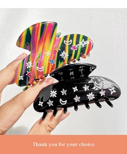 Detail showing two luxury hair claws with star and moon patterns in black and rainbow