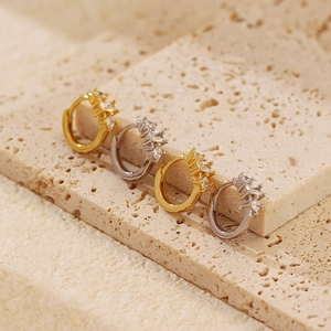 Close-up of gold and silver S925 earrings with geometric zircons on a beige stone