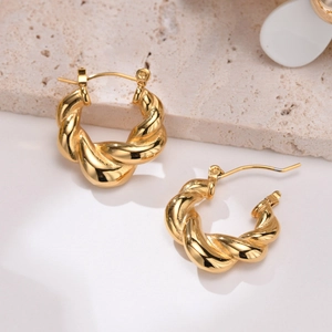 Detail of gold twisted hoop earrings showing high-gloss texture on travertine stone