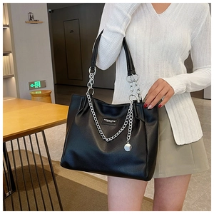Detail of black pebbled leather tote bag with silver chain strap shown on shoulder