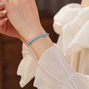 Detail of turquoise beaded bracelet with heart pendant and silver crystal charm on wrist