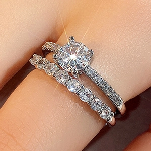 Close-up of elegant silver ring set with six-prong solitaire and pavé band on a finger
