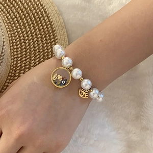 Detailed shot of pearl bracelet with Evil Eye and Hamsa Hand charms on white fur