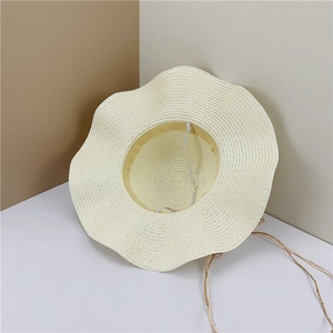 Close-up of beige woven straw sun hat showing wave brim texture and decorative cord detail