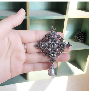 Detailed view of a vintage Baroque silver cross brooch with dark stones and pearl drop