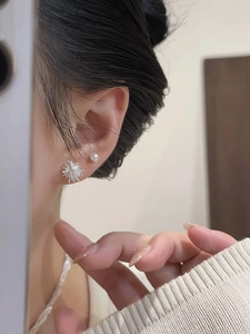 Macro side view of silver dandelion and pearl studs on model ear for elegant style