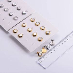 Detailed view of gold and silver shell stud earrings with a ruler for size reference
