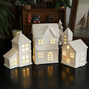 Three white ceramic Christmas house ornaments with warm LED lights in a cozy home setting