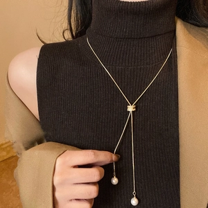 Collier en Y doré avec pendentifs en perles blanches sur un pull à col roulé noir
