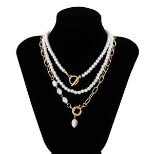 Detail of layered gold chain and pearl necklace with T-bar clasp on a black bust display