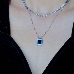 Detail of layered silver necklaces with a black rectangular pendant on a neck