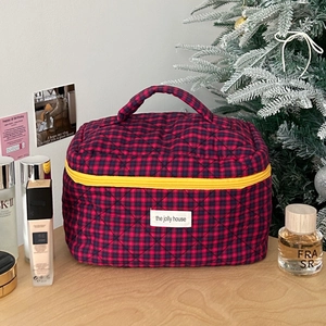 Close-up of red and blue checkered quilted cosmetic bag with yellow zipper on wooden table