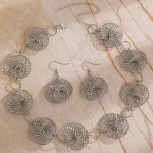 Detail shot of silver hollow spiral sphere necklace and earrings on textured stone