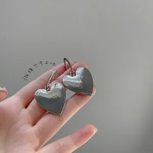 Detail of silver hammered heart earrings with twisted rope hoops held in hand