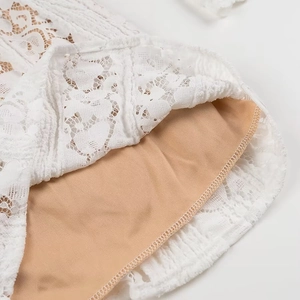 Detailaufnahme von weißem Spitzenstoff mit nudefarbenem Futter an einem Mini-Kleid