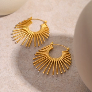 Macro shot of 18k gold fan-shaped earrings with rhinestones on beige stone texture