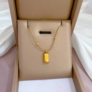 Detail of a gold rectangular bar pendant on a snake chain inside a beige jewelry box