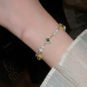 Elegant gold bracelet with green zircons and white pearls worn by a model in lace