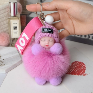 Detail of pink fox fur puff ball keychain with sleeping baby doll and knitted hat