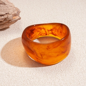 Macro shot of wide amber resin bangle with unique brown swirled textures on a beige stone