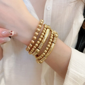 Détail de bracelets à perles dorées et joncs en métal portés sur un poignet