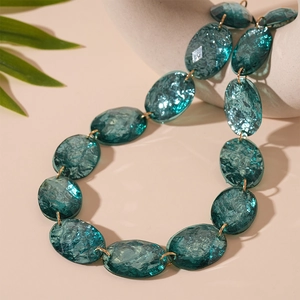 Macro detail of oval peacock blue resin beads with ice crackle texture on gold chain