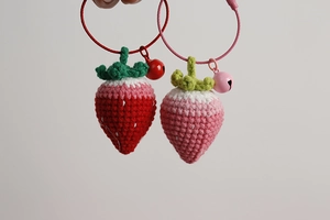 Close-up of handmade crochet strawberry charms in pink and red with matching bells