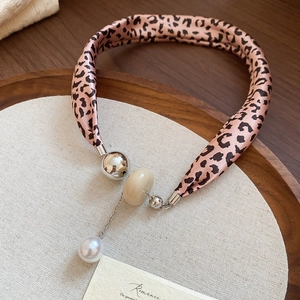 Détail du collier foulard en soie léopard rose avec breloques perles sur plateau en bois