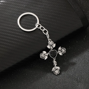Detailed silver metal gothic cross keychain with rose and black heart gemstone on carbon surface