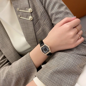 Close-up of luxury tonneau gold watch with diamond bezel and black leather strap